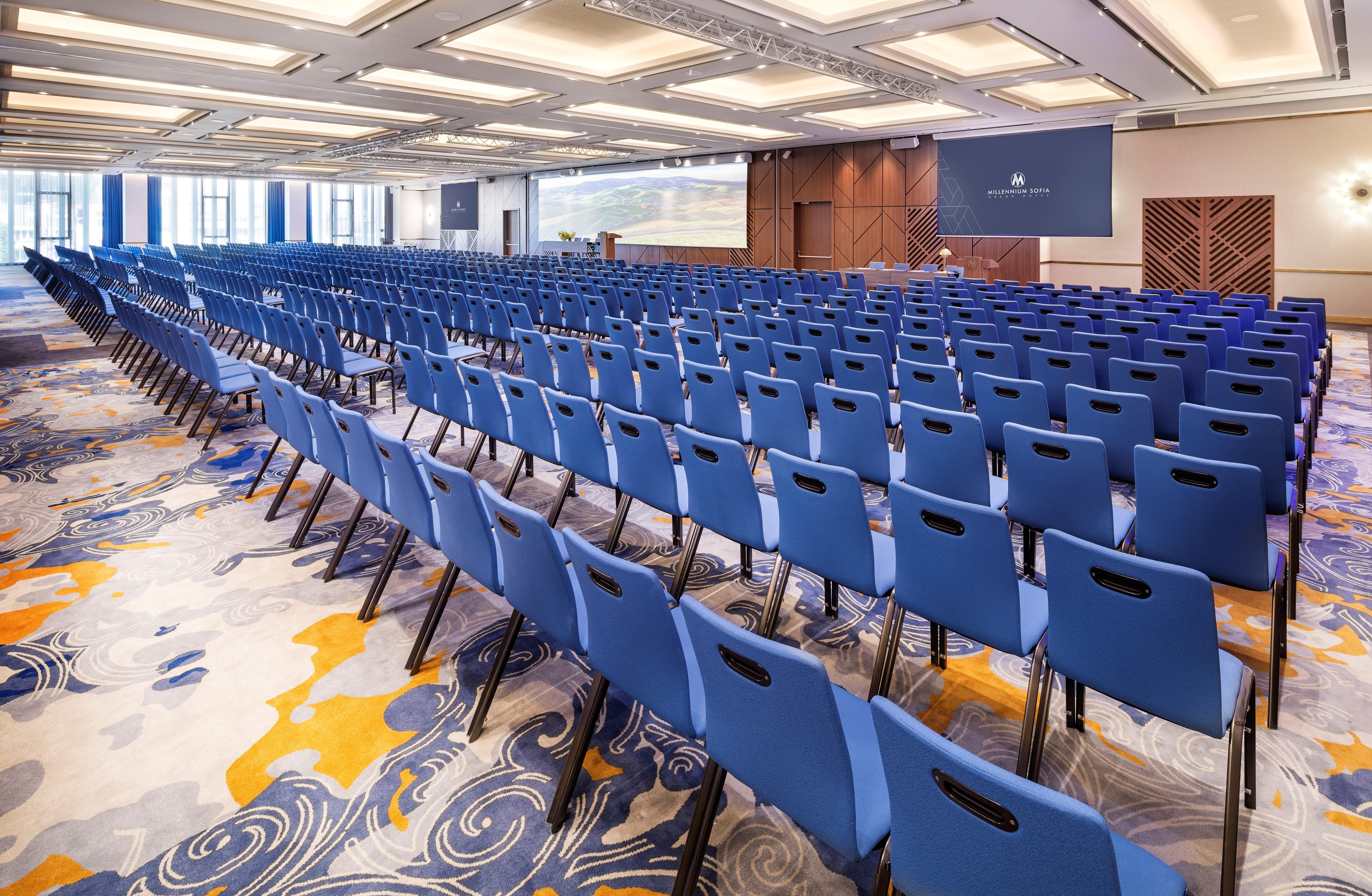 Grand Hotel Millennium Софія Екстер'єр фото The photo shows a large conference or meeting room set up for an event. There are numerous blue chairs arranged in rows, creating a seating area for attendees. The floor features a decorative pattern, and the room has a modern design with ample light