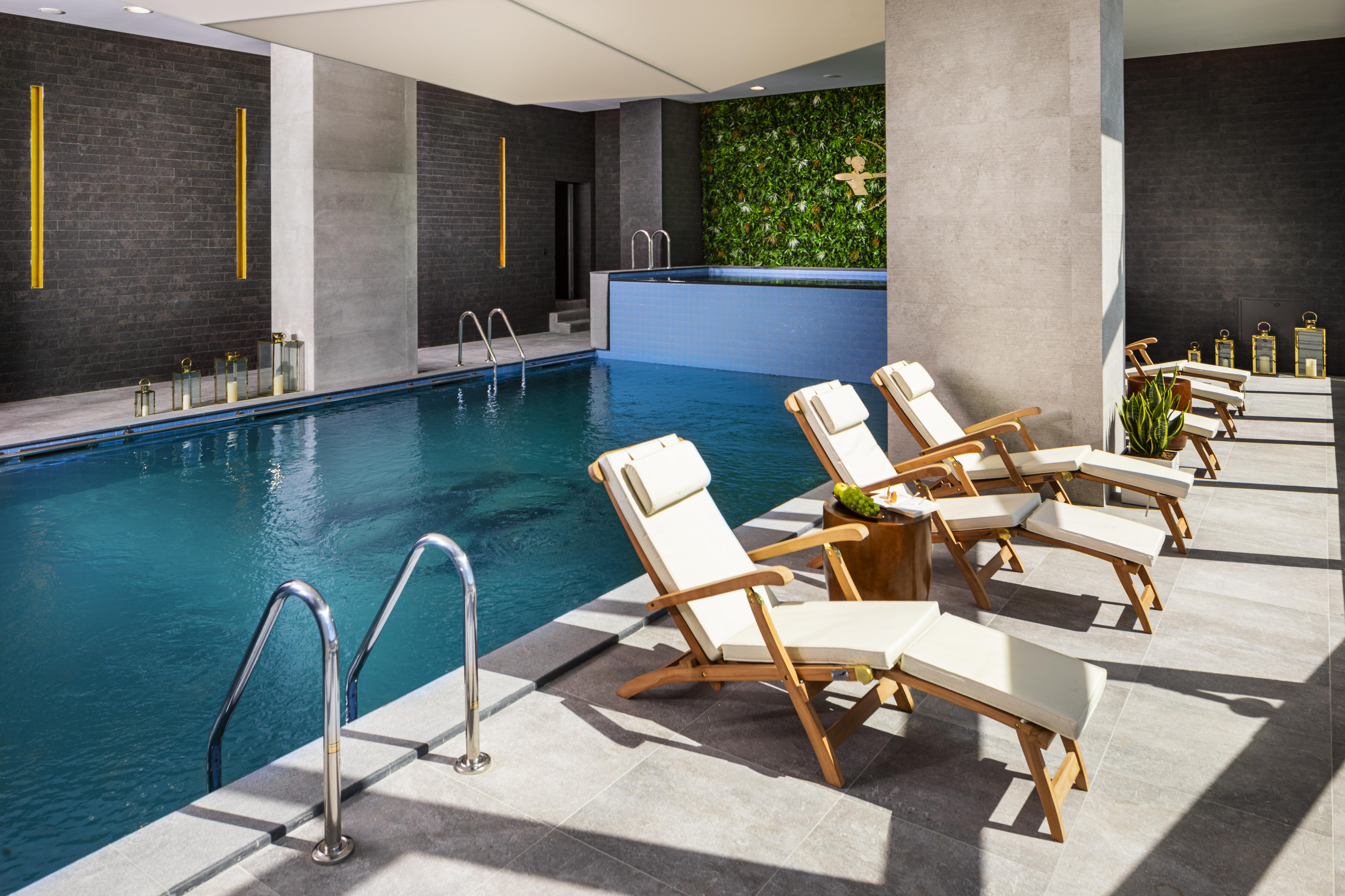Grand Hotel Millennium Софія Екстер'єр фото The photo shows a serene indoor swimming pool area. The pool is clear and inviting, with a blue water surface reflecting light. Along one side of the pool, there are several light-colored lounge chairs with white cushions, positioned for relaxation. 